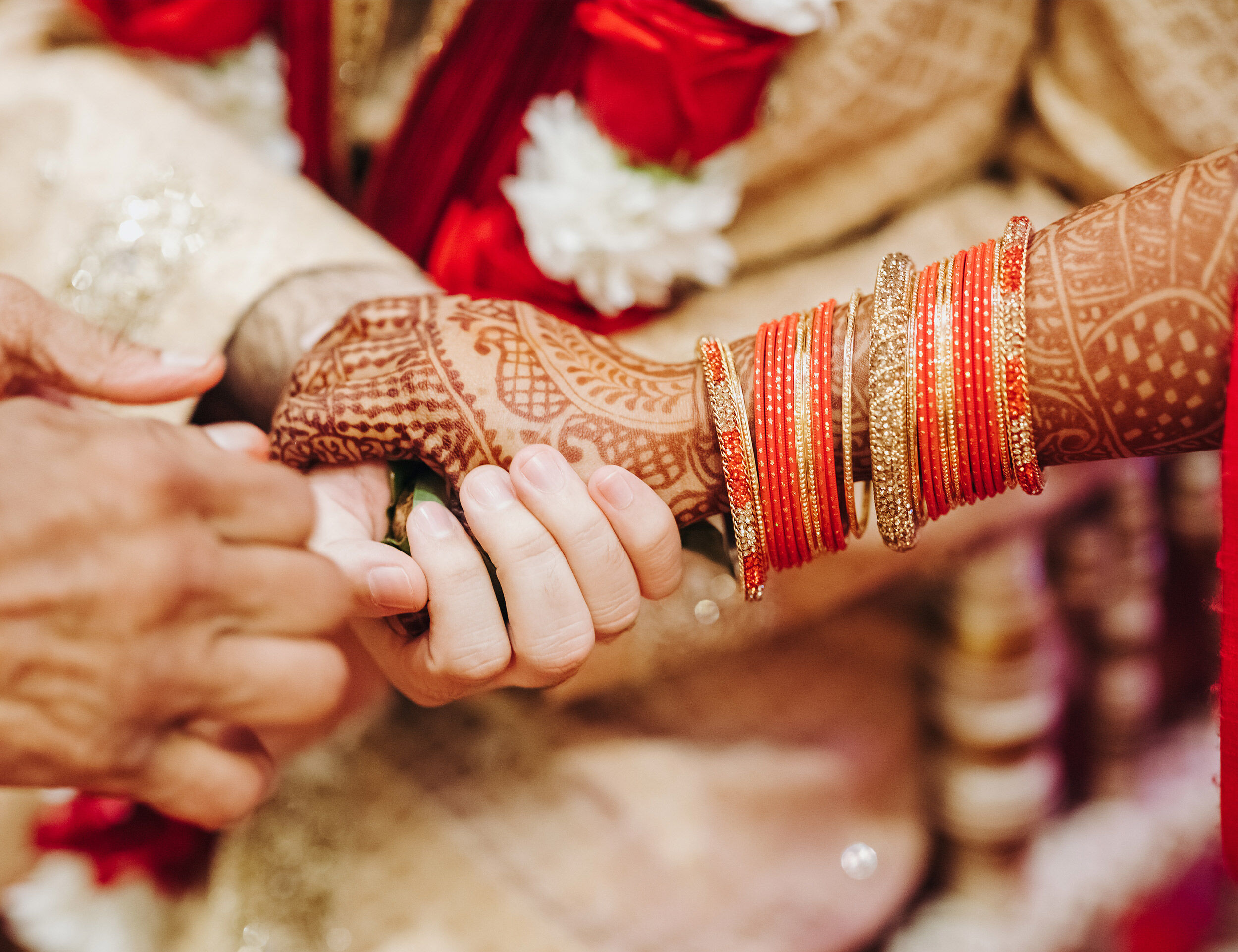Bride and groom exchanging sacred vows with hands adorned with red chooda bangles and intricate mehndi designs during the Punjabi wedding ceremony